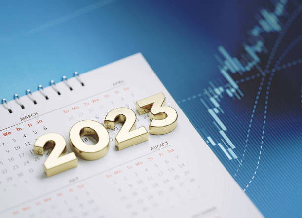 Gold colored 2023 sitting over a white calendar on blue financial graph. Horizontal composition with selective focus and copy space. Investment, stock market data and financial planning concept.
