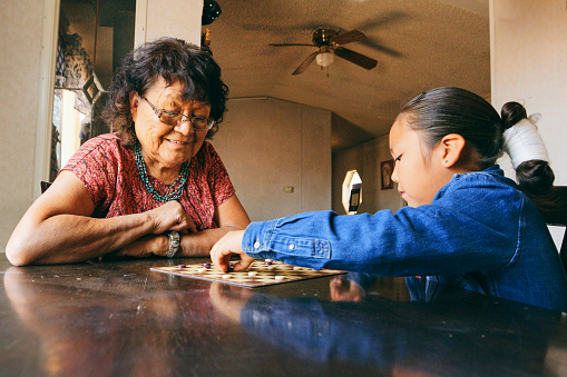An Indigenous Navajo grandmother, playing a game of checkers in a home with her grandson.