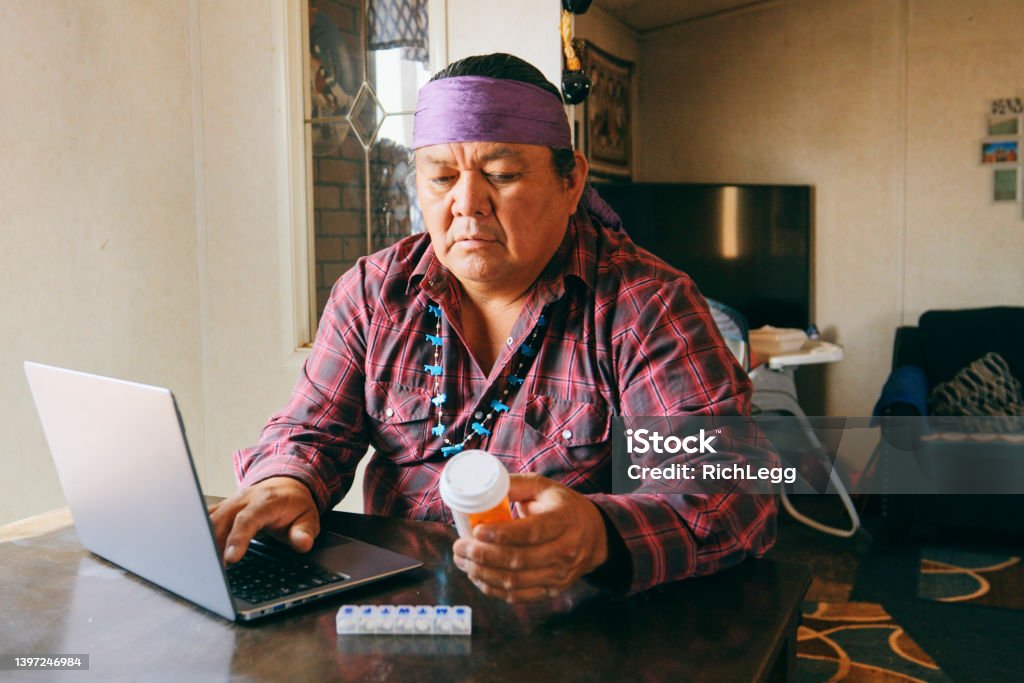 Mature Man Filling Medicine Prescription Online A mature Indigenous Navajo man, refilling a medicine prescription online from home with a laptop computer. Indigenous Peoples of the Americas Stock Photo