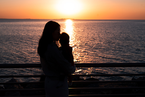 Asian woman hugging her baby boy by the seaside on the beach on a summer vacation backlit silhouette. Mother and son on the seaside spending time outdoors