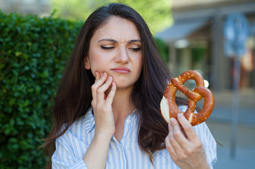 Young woman with a pretzel in hand having toothache