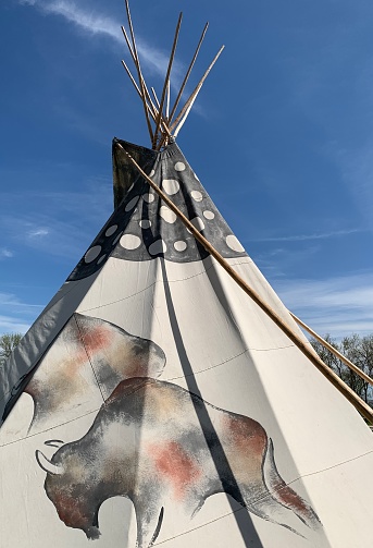 Indigenous Dakota tipi (teepee) with painted buffalo and circles against blue sky