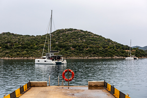 Orange color lifebuoy hanging by the sea. Catamaran sailboat can be seen in the background.