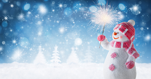 Happy snowman snowman holding sparkler on a snowy winter night. Christmas or New Year panoramic background or greeting card. Fabulous winter composition with snowman dressed in warm clothes, mittens, scarf and hat.