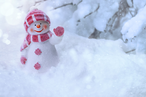 Happy snowman standing in winter landscape. Merry Christmas and Happy New Year greeting card with copy space. Snowman dressed in warm clothes, mittens, scarf and hat and snow on background. Winter fairytale.