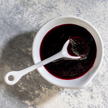 Close-up blueberry sauce and serving spoon in small white porcelain bowl on gray background.