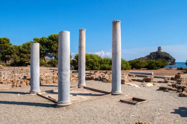 Excavations and remains of old columns with a tower in the background near the town of Nora on the island of Sardinia