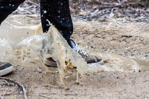 Closeup walking through mud puddle with large water splash, background with copy space, full frame horizontal composition