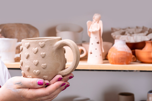 Close up of female potter hands holding clay cup handcraft crockery in studio.