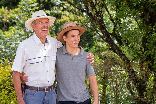 Father and son spending time together cuddling side by side while laughing together. Father and son latin farm workers wearing hats together on a hot day.