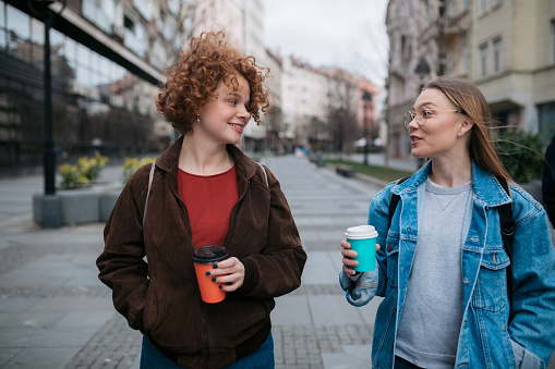 Two happy female friends meeting for a cup of coffee, walking through the city, talking and socializing