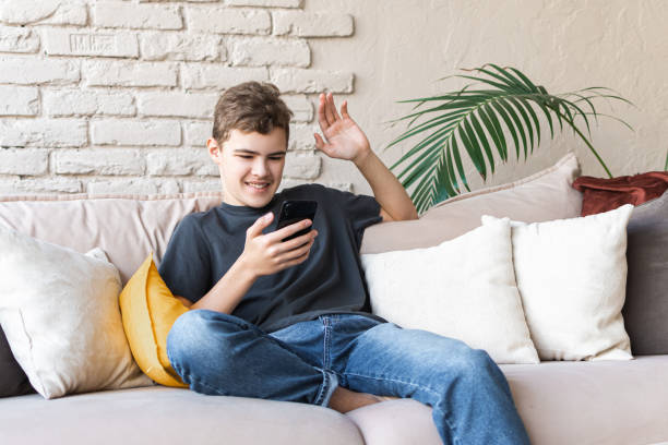istock A smiling teenage boy with a smartphone in his hands communicates with peers using a smartphone and waves his hand in a video chat. Distance learning and communication 1397270437