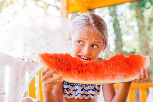 여름 테라스에있는 소녀는 붉은 수박과 미소의 큰 조각을 먹는다. 음식 자연. 여름에 잘 익은 육즙이 많은 수박을 먹는 소녀. 사랑스러운 금발 소녀는 야외에서 수박 조각을 먹습니다. - watermelon missing bite melon grass 뉴스 사진 이미지