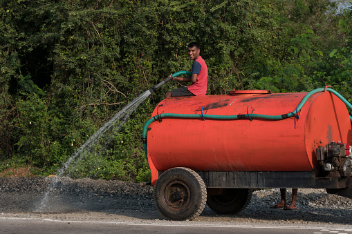 Unawatuna, Sri Lanka March 25, 2022 A man sits atop a red water truck and waters the road down.