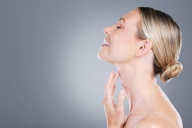 studio shot of an attractive mature woman touching her neck against a grey background - touching neck imagens e fotografias de stock