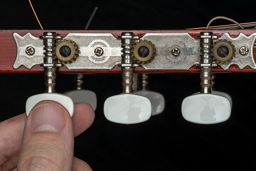 CLOSE UP OF A MALE HAND TUNING GUITAR PEGS ON HEADSTOCK.