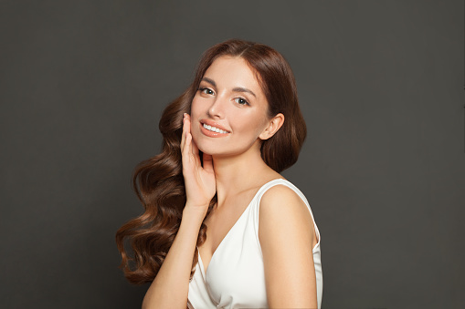 Portrait of young brown haired woman  with voluminous, shiny and wavy hair. Elegant makeup with black mascara and rose lipstick on her face. Beautiful model with long, dense and curly hairstyle.