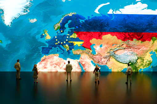 Businessman/politician figurines examine satellite view European Union, Ukraine and Russia maps.