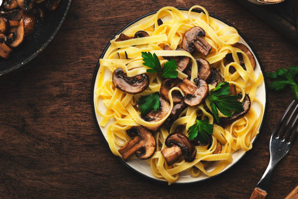 massa de fettuccine saborosa com cogumelos servidos no prato com verduras e tempero na mesa de madeira rústica fundo da mesa de madeira, vista superior. cozinha vegetariana saudável e alimentação. conceito de comida italiana - close up table brown dieting - fotografias e filmes do acervo