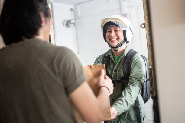 Asian Chinese Food Delivery Person with a motorcycle helmet sends food to a residence stock photo