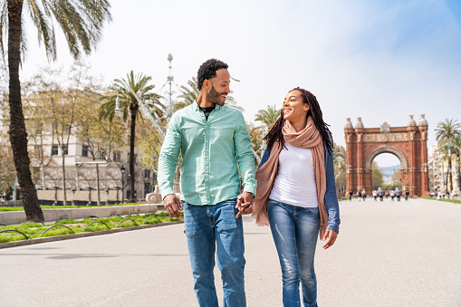 Beautiful happy hispanic latino couple of lovers dating outdoors - Tourists in Barcelona having fun during summer vacation and visiting Arc de Triumf historic landmark