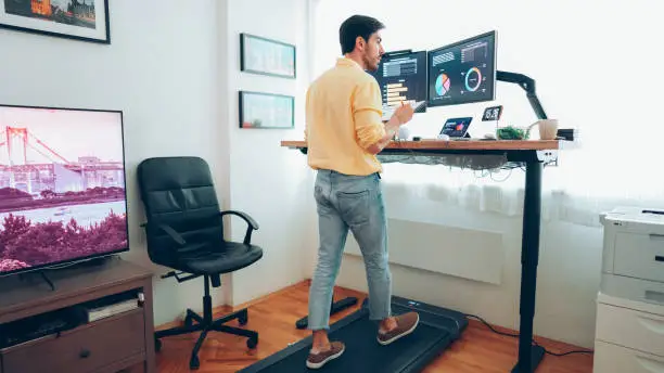 Man working from home at standing desk is walking on under desk treadmill