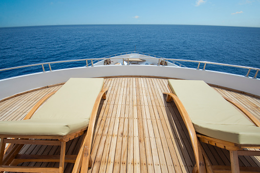 Teak bow sundeck of a large luxury motor yacht out at sea with sunbeds and a tropical ocean view background