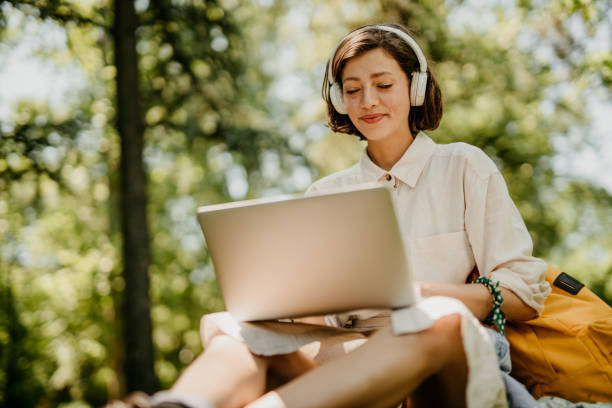 Close up of a college girl on a video call sitting in a park. Beautiful girl doing a video chat using a laptop computer and headphones sitting outdoors.