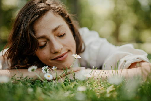 Low angle view of a beautiful young woman lying down in the grass, and smelling the white flowers. Nature, taking care concept