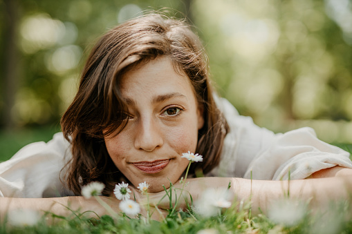 Low angle view of a beautiful young woman lying down in the grass, and smelling the white flowers. Nature, taking care concept