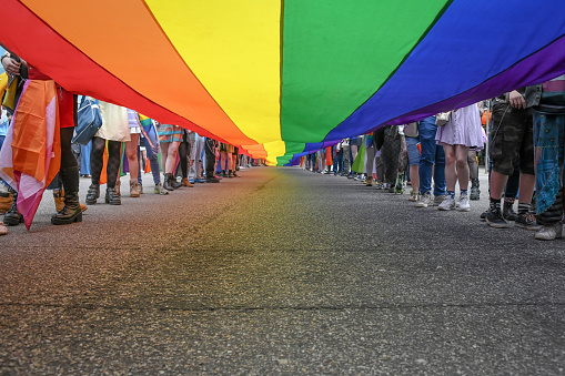 Under a LGBT Pride Flag with the legs of people carrying the flag