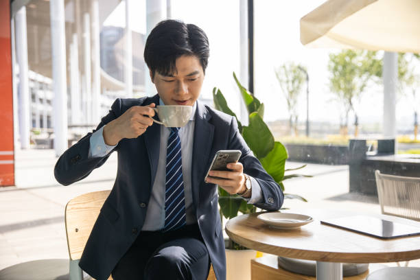 istock Asian businessman using phone and drinking coffee at a cafe 1397330998
