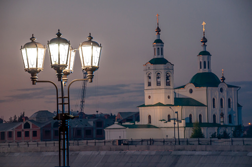 Street lights are located on the streets of the city on the background with a church. Street lights are illuminating everything around the black night