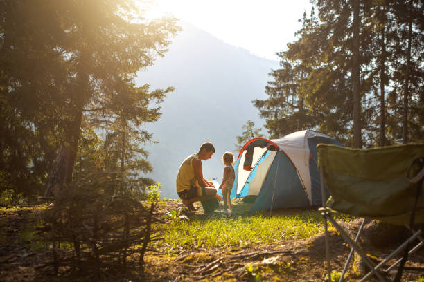 Dad and daughter of 2 years old near a tent in a camping in the forest in the mountains.Family outdoor recreation, eco-friendly adventures, survival in the wild. stock photo