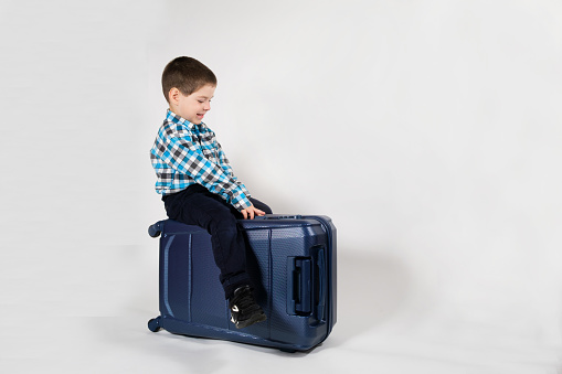 A 4-year-old boy sits on a blue travel suitcase on a white background with space for text