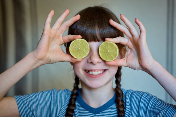 little girl holding half a lemon in her eyes. Healthy happiness stock photo