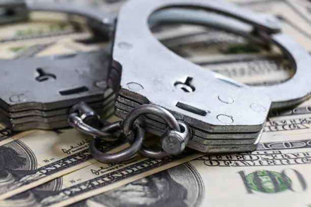 Photo of Cash in US Dollars, Real Handcuffs. The Concept of Arrest, Corruption, Bail, Crime, Bribery or Fraud.