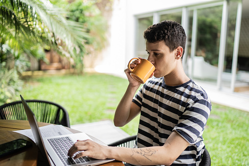 Young man drinking coffee while using laptop in the backyard