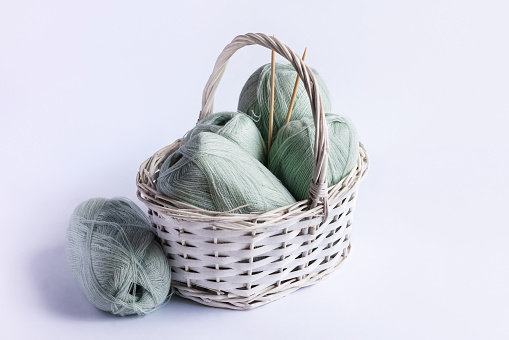Light green yarn threads in a white basket on a blue background with knitting needles.