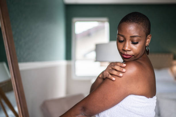 Woman wearing a towel applying moisturizer Woman wearing a towel applying moisturizer black skin stock pictures, royalty-free photos & images