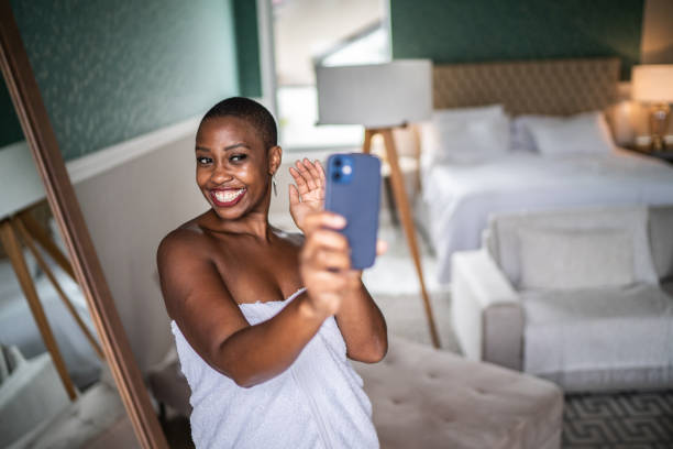 Woman using mobile phone doing a video call (or taking a selfie) wearing a towel at home