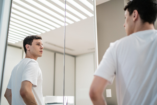 Full length profile shot of a young man getting ready and looking at a mirror isolated on white background