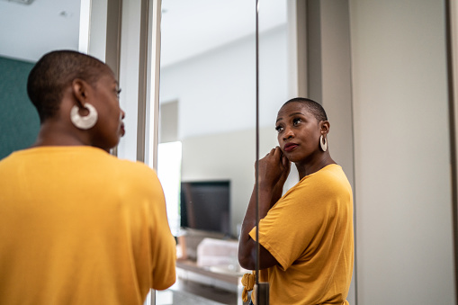 Mid adult woman putting on earrings looking in the mirror at home