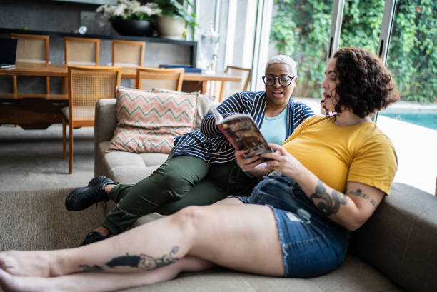 mid adult woman talking with a friend and reading a book at home - women common 40s candid imagens e fotografias de stock