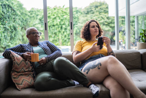Female friends watching TV and using mobile phone at home