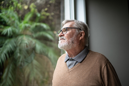 Contemplative senior man looking through window at home