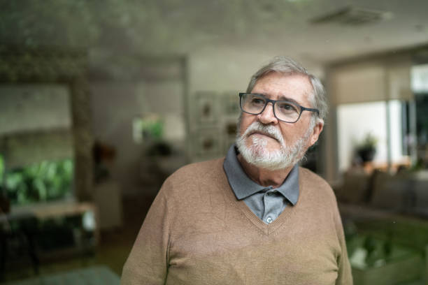 Contemplative senior man looking through window at home