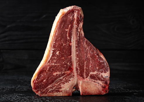 Raw T Bone beef steak with herb and seasoning on rustic background.