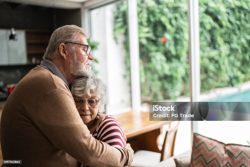 Senior couple hugging each other at home Embracing Stock Photo
