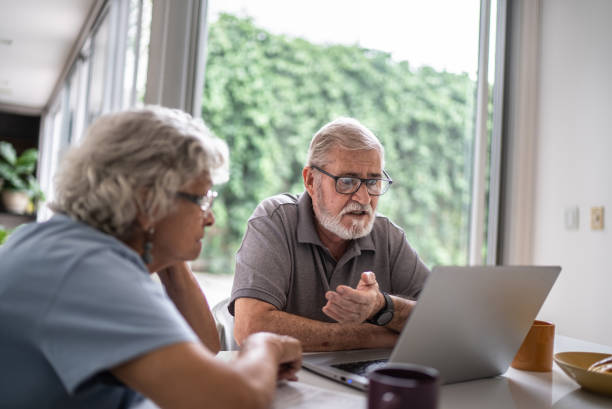 älteres paar, das über hausfinanzen spricht und den laptop zu hause benutzt - couple senior adult sadness emotional stress stock-fotos und bilder